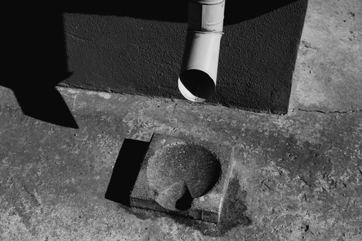 Black and white photo of a concrete drainage with sunlight casting shadows on pavement.