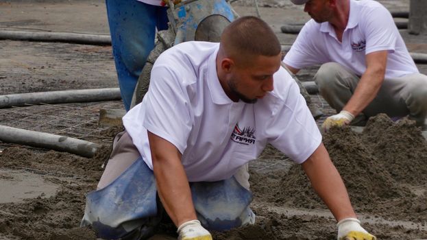 Construction workers expertly level wet concrete for a smooth finish on a building site.